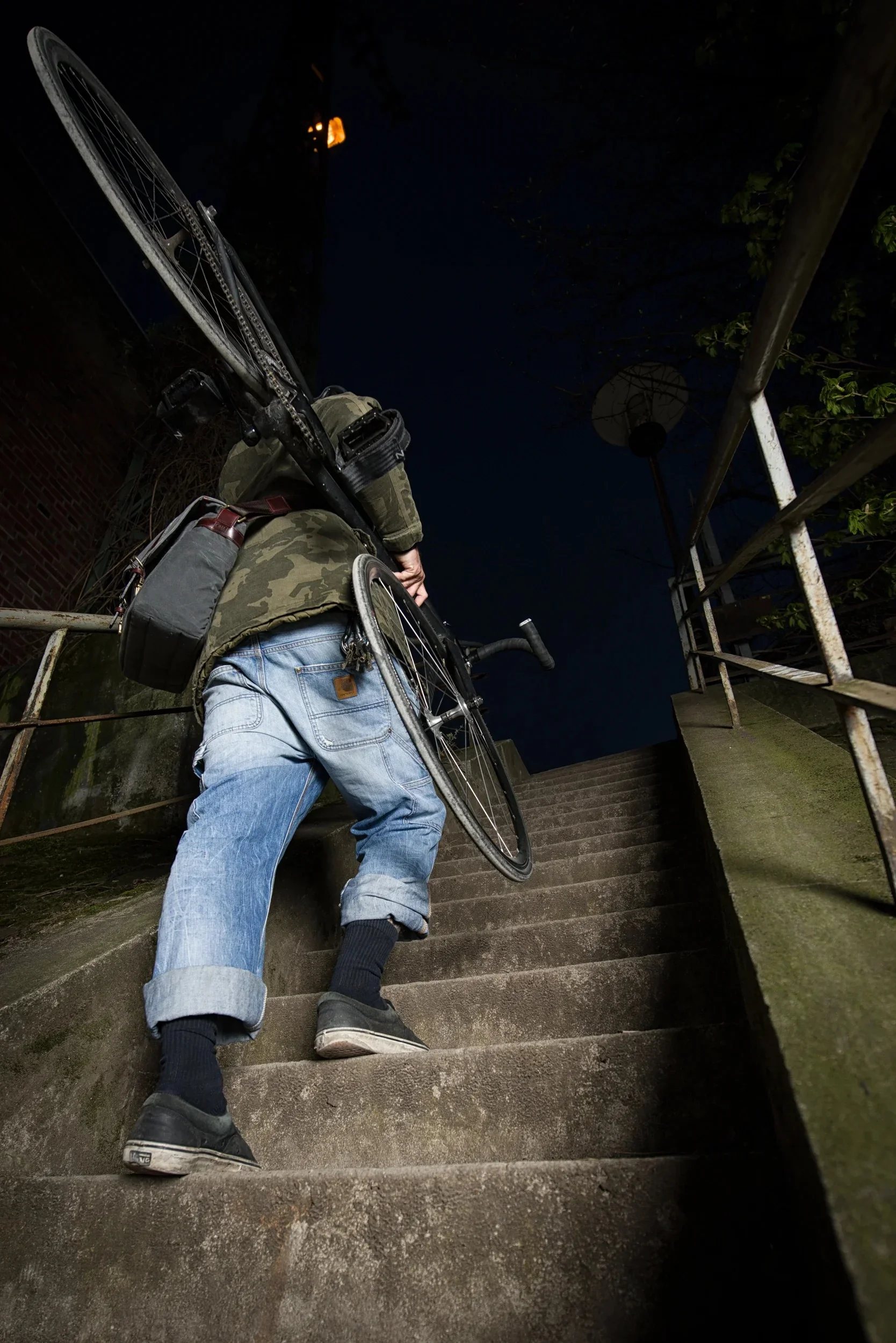 Low-angle shot of a cyclist carrying their bike up urban stairs at night.